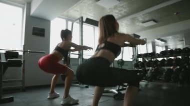 Spor giyim sektöründe iki aktif bayan arkadaşın modern spor salonunda güçlü kalçaları için çömelme egzersizleri yapmaları. Fitness kızları sağlıklı ve formda olmak için düzenli olarak antrenman yaparlar..