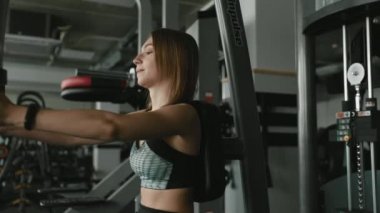 Spor giyim kuşağında koyu renk saçlı kendine güvenen fitness kızı spor yaparken kaslarını çalıştırmak için spor simülatörü kullanıyor. Güç kavramı, öz disiplin ve sağlıklı yaşam tarzı..