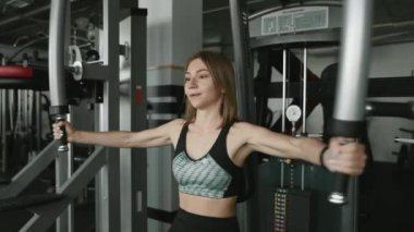 Spor giyim kuşağında koyu renk saçlı kendine güvenen fitness kızı spor yaparken kaslarını çalıştırmak için spor simülatörü kullanıyor. Güç kavramı, öz disiplin ve sağlıklı yaşam tarzı..