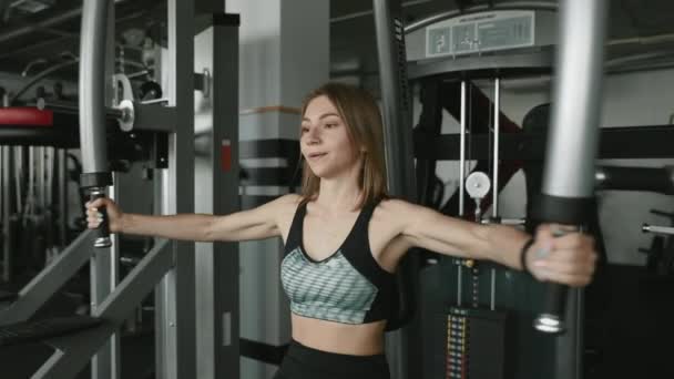 운동복 차림의 머리의 신축성있는 소녀는 정기적으로 운동을 근육에 체육관 시뮬레이터를 — 비디오
