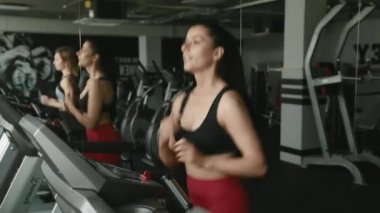 Spor kıyafetleriyle spor salonunda koşu bandında koşan iki mutlu aktif kız. Güzel bayan arkadaşlar sohbet ediyor ve birlikte kardiyo yapıyorlar. Dayanıklılık ve motivasyon kavramı.