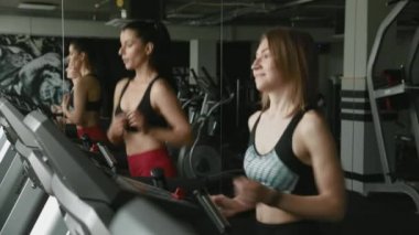 Spor kıyafetleriyle spor salonunda koşu bandında koşan iki mutlu aktif kız. Güzel bayan arkadaşlar sohbet ediyor ve birlikte kardiyo yapıyorlar. Dayanıklılık ve motivasyon kavramı.