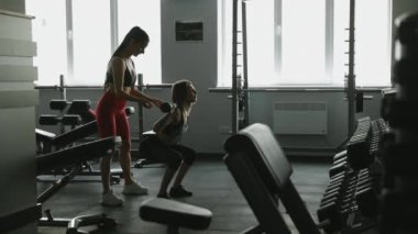 Ağır halterle çömelme hareketleri sırasında kadın müşterisini kontrol eden sağlıklı spor koçu. Güzel bir kadın spor salonunda profesyonel antrenörle çalışıyor..