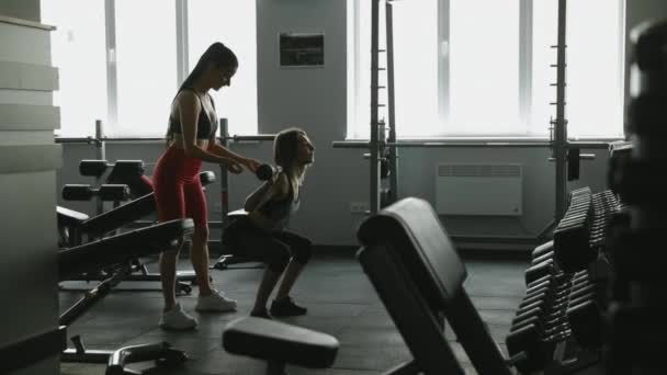 迷人的健身教练穿着运动服 在她的女客户表演时 用沉重的杠铃控制她的女客户 有职业教练在体育馆做漂亮的女子锻炼 — 图库视频影像