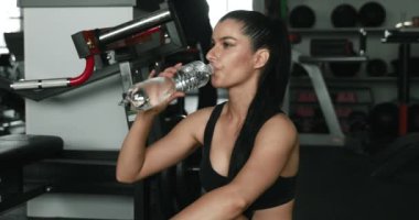 Spor sutyen ve taytlı, spor salonunda mola verirken temiz su içen yorgun, genç bir esmer. Koyu saçlı aktif bir kadın antrenman sırasında dinlendirici ve ferahlatıcı..