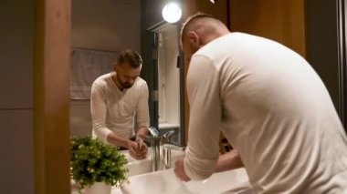 Beyaz gömlekli sorumluluk sahibi adamın ellerini lavaboda akan suyun altında sabunla yıkaması. Hijyen, sağlık ve önleme kavramı.