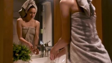 Beyaz lavaboda ellerini sabunla yıkayan terli havluyla göz kamaştırıcı genç bir bayan. Modern banyodaki aynada yansıması. Sabah rutini ve hijyen anlayışı.