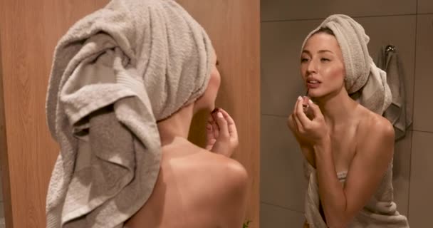 Frau im Handtuch blickt in Spiegel und trägt Lippenstift auf — Stockvideo
