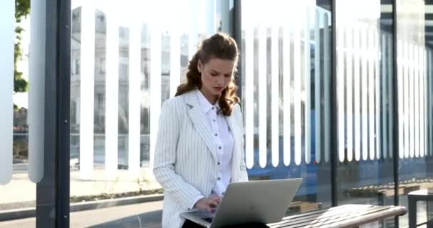 Mooie vrouw werken op laptop terwijl zitten op bushalte — Stockvideo