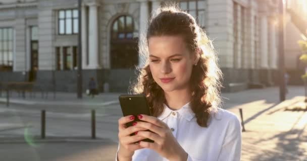 Retrato de niña sonriente de pie en la calle con teléfono inteligente — Vídeos de Stock