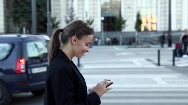 Otobüs durağında toplu taşıma beklerken günlük kıyafet giymiş mutlu genç bir kadın şehirde gezinmek için başvuruda bulunuyor. Güzel kız internette akıllı telefondan temiz havada geziniyor..