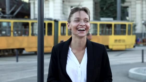 Charmante jeune femme aux cheveux foncés en tenue décontractée debout à la gare routière et regardant la caméra avec un sourire sincère. Concept d'espace urbain et d'émotion humaine réelle. — Video