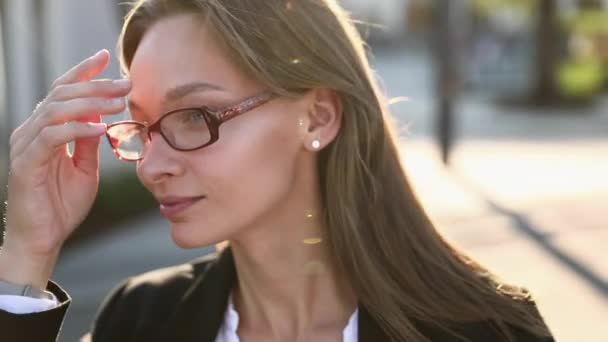 Mosolygós, sikeres nő portréja szemüvegben és üzleti öltönyben, ahogy az irodaház közelében áll és a kamerába néz. Magabiztos nő természetes szépség pózol az utcán. — Stock videók