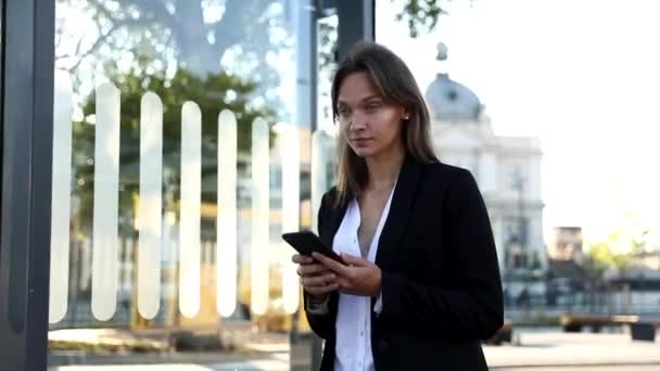 Atractiva mujer de cabello oscuro con camisa blanca y chaqueta negra usando smartphone para comprobar la ubicación en la gran ciudad. Concepto de personas, navegación y tecnología. — Vídeos de Stock