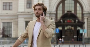 Ciddi bir yüz ifadesi olan sakallı iş adamı dışarıda dikiliyor ve akıllı telefondan konuşuyor. Resmi kıyafetler içinde yakışıklı bir adam. Mesafe sorunlarını çözüyor..