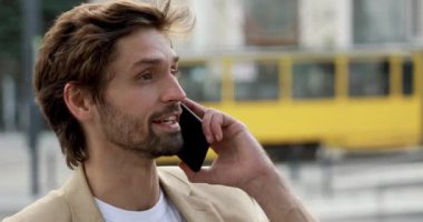Resmi kıyafetli duygusal sakallı bir adam akıllı telefondan iş görüşmesi yapıyor. Yakışıklı erkek dışarıda dururken eşleriyle telefonda konuşuyor..