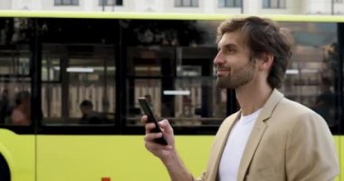 Takım elbiseli mutlu yakışıklı adam akıllı telefondan toplu taşıma zamanını kontrol ediyor. Sakallı adam otobüs bekliyor ve modern bir cihaz kullanıyor..