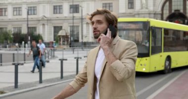 Resmi takım elbiseli yakışıklı adam elinde bavulla otobüs durağında duruyor ve akıllı telefondan ortaklarıyla konuşuyor. Genç adam iş gezisi sırasında iş görüşmesi yapıyor..