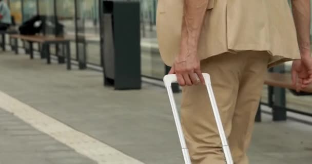 Primer plano del hombre de negocios en ropa formal que lleva en maleta blanca mientras camina en la parada de autobús. Joven disfrutando de viajar durante el tiempo de trabajo. — Vídeo de stock