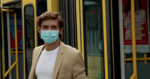 Portret van een knappe man met een medisch masker en een formeel pak die uit de tram stapt. Baard man beschermt zichzelf tegen virus in het openbaar vervoer. — Stockvideo
