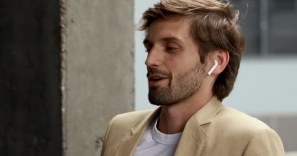 Retrato de hombre barbudo confiado usando auriculares inalámbricos para conversación de trabajo. Joven hombre de negocios en ropa formal haciendo su trabajo a distancia. — Vídeos de Stock