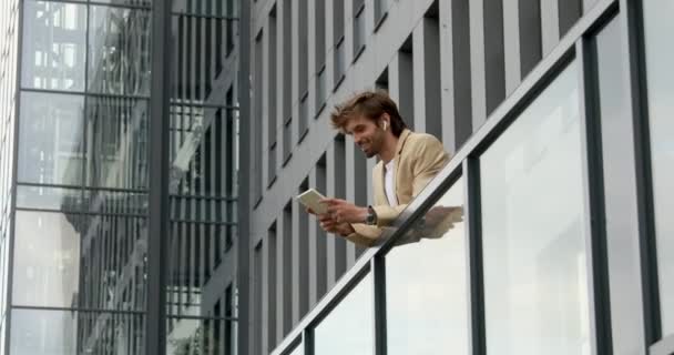Vista lateral do homem barbudo alegre em terno de negócios em pé na varanda do centro de escritório e segurando tablet digital. Conceito de gadget moderno e carreira de sucesso. — Vídeo de Stock