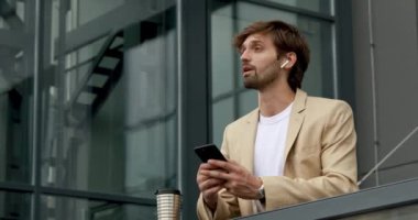 Kendine güvenen, resmi giyinmiş, akıllı telefondan modern kulaklıkları kullanan yakışıklı bir adam. Sakallı adam dışarıda dururken telefonda ortaklarıyla konuşuyor..