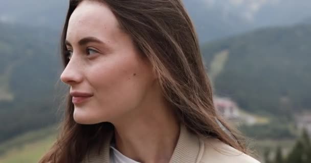Close-up van jonge vrouw in blauwe regenjas die vrije tijd doorbrengt om naar de bergen te reizen. gelukkig meisje met bruin haar staan op de top van heuvel na regen. — Stockvideo