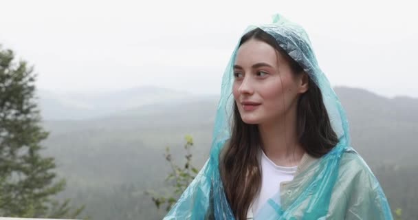 Mujer morena satisfecha vestida con impermeable azul disfrutando de la hermosa naturaleza entre las montañas. Concepto de viaje, turismo y placer. — Vídeos de Stock
