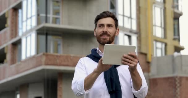 Hombre guapo en camisa blanca haciendo gesto ganador y sintiéndose feliz debido a la realización exitosa nuevo proyecto de arquitectura. barbudo chico de pie al aire libre y el uso de gadget digital. — Vídeos de Stock