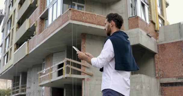 남자 건축가가 건설 공정을 통제하기 위해 디지털 가젯을 고소하는 모습. 밖에서 현대식 기구를 들고 있는 수염을 기른 남자. — 비디오