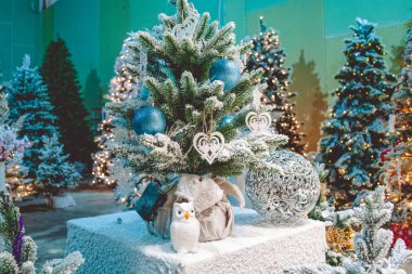 Küçük Noel ağacı güzel yılbaşı oyuncakları ve kapak sahte kar ile süslenmiş. Beyaz baykuş ve yakınındaki figürlü küre. Arka plan ışıkları garland ile büyük Noel ağaçları.