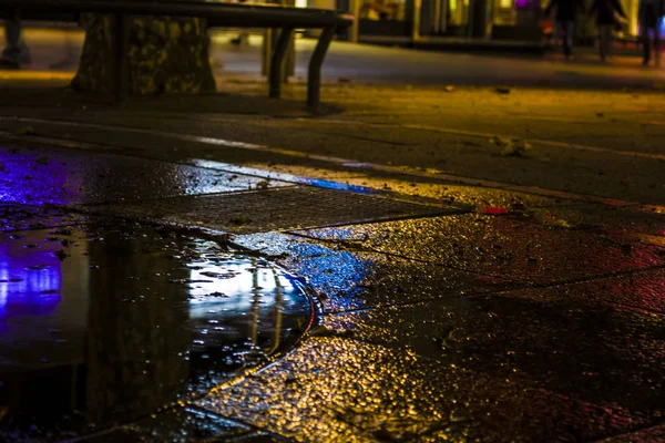 Lichtflecken und Reflexionen von Feuern der nächtlichen Stadt in einer feuchten Fliese auf der Straße — Stockfoto