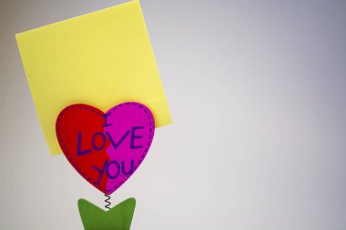 Beyaz arka plan. Ahşap kalp bir clothespeg için bir bahar üzerinde sopa ile. Kutlama. St. Valentine's Day. Sarı kağıt. 