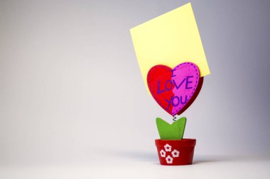 Beyaz arka plan. Ahşap kalp bir clothespeg için bir bahar üzerinde sopa ile. Kutlama. Davet. St. Valentine's Day. Sarı kağıt. Yazıt ile 