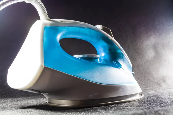 The blue iron for ironing of clothes. Monophonic black background. Household appliances. Electronics. Modern technologies. — Stock Photo, Image
