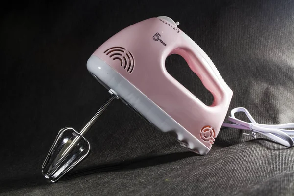 Home electric mixer of pink and white colors. On a monophonic black background. Nozzles for the mixer. Modern technologies.