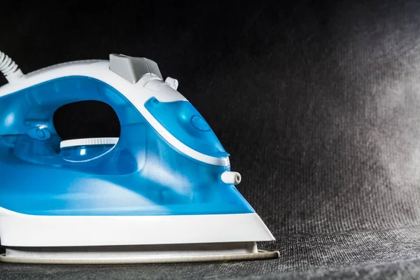 The electric blue iron with white color. Modern small appliances for the house. Ironing. Black background.