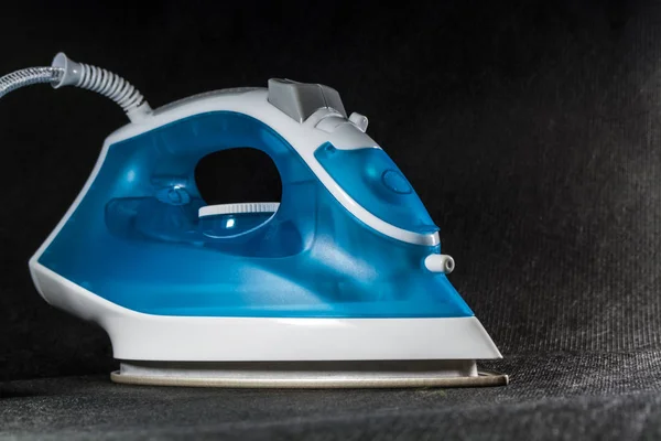 The electric blue iron with white color. Modern small appliances for the house. Ironing. Black background.