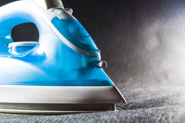 The electric blue iron with white color. Modern small appliances for the house. Ironing. Black background.