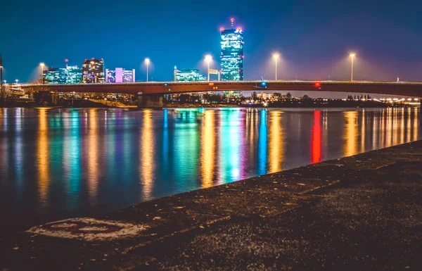 Βράδυ πολύχρωμα πυρκαγιές από σύγχρονες ουρανοξύστες και η γέφυρα στη Βιέννη αντικατοπτρίζονται στο ποτάμι. Όμορφη θέα. Τοπίο — Φωτογραφία Αρχείου