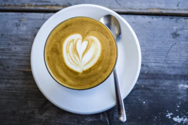 Dicke Glasbecher mit Cappuccino und Latte-Art in Herzform. frischen Kaffee mit Milch. auf einem Holztisch mit Untertasse, Löffel — Stockfoto
