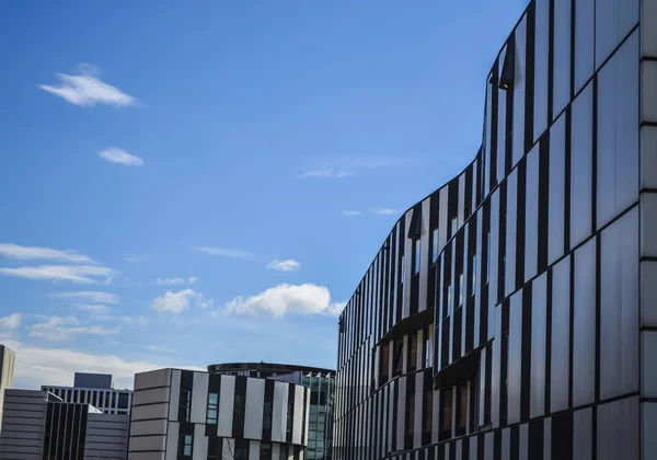 Modern buildings of unusual forms from glass and metal. Geometry of lines and curves. The inclined facade. Blue sky.