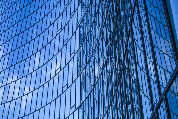 Modern architecture of office buildings. A skyscraper from glass and metal in the form of a curved wave. Reflections in windows of the blue sky and houses. Business center. — Stock Photo, Image
