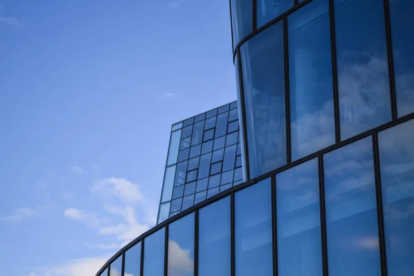 Arquitectura moderna de edificios de oficinas. Un rascacielos de vidrio y metal en forma de ola curva. Reflejos en ventanas del cielo azul y casas. Centro de negocios . — Foto de Stock