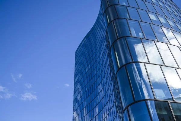 Arquitectura moderna de edificios de oficinas. Un rascacielos de vidrio y metal en forma de ola curva. Reflejos en ventanas del cielo azul y casas. Centro de negocios . — Foto de Stock