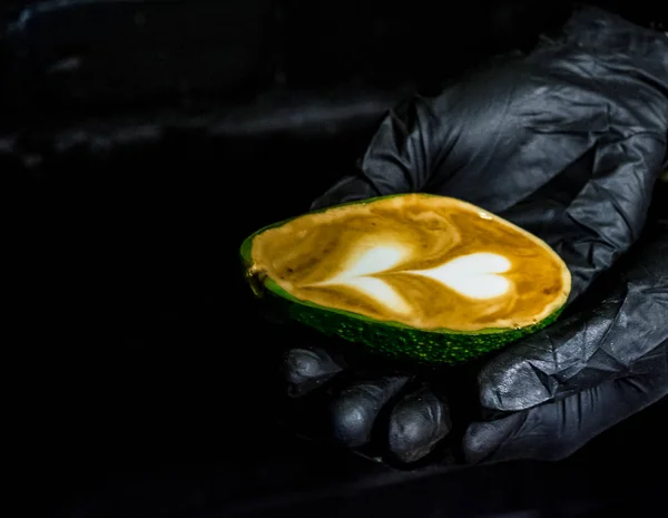 Hände in schwarzen Handschuhen und darin ein Cappuccino mit Latte Art in Avocado. Ungewöhnlicher Pokal. frischer und schöner Kaffee mit Milch. — Stockfoto