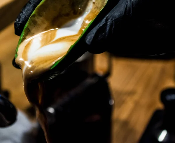 Cappuccino, latte a művészet avokádó kiömlik a barista a fekete kesztyűt. Szokatlan kupa. Friss és szép kávé tejjel — Stock Fotó