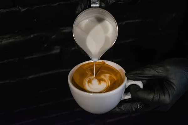 Cappuccino, latte art elkészítése folyamata. Munka a barista kávézóban. Fekete háttér és a kesztyűt. Friss kávé — Stock Fotó