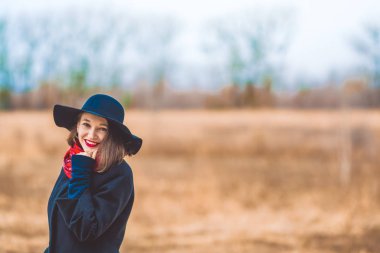 Genç kız bir siyah palto ve şapka boş alana baharda yürür. Kırmızı ruj dudakları ve bir gülümseme. Moda ve stil